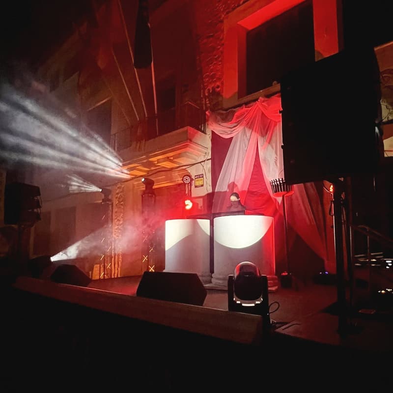 DJ en una plaça de poble de Mallorca amb feixos de llum, fum i sistema de so a l'escenari